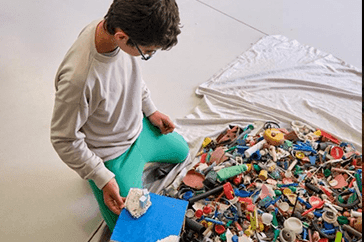 Young person sorting marine litter indoors, during a workshop for marine pollution reduction and behavioral change to protect Portugal’s ocean and coastal ecosystems.